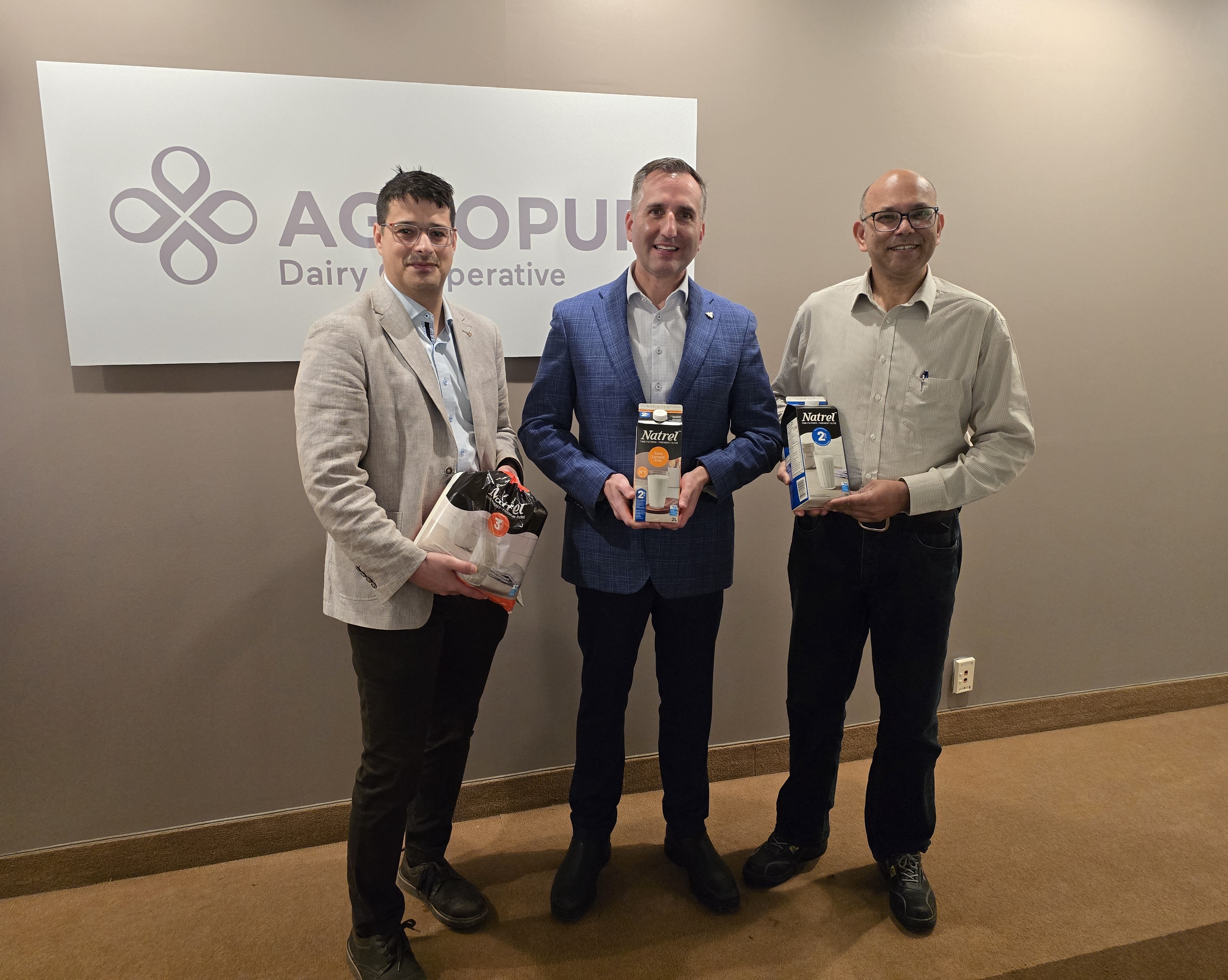 Three men holding Natrel dairy products in front of the Agropur logo