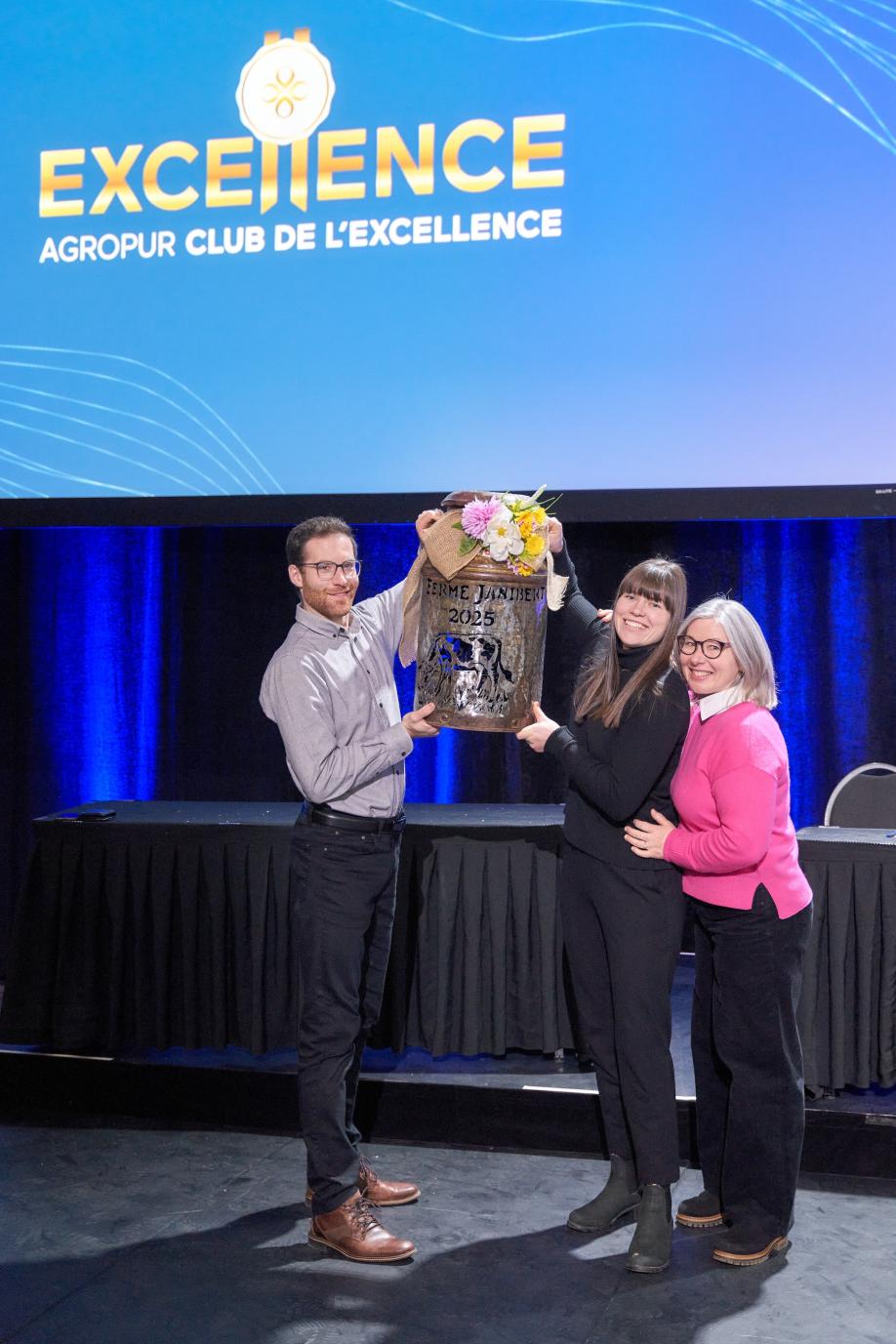 a man and two women holding up a trophy on a stage