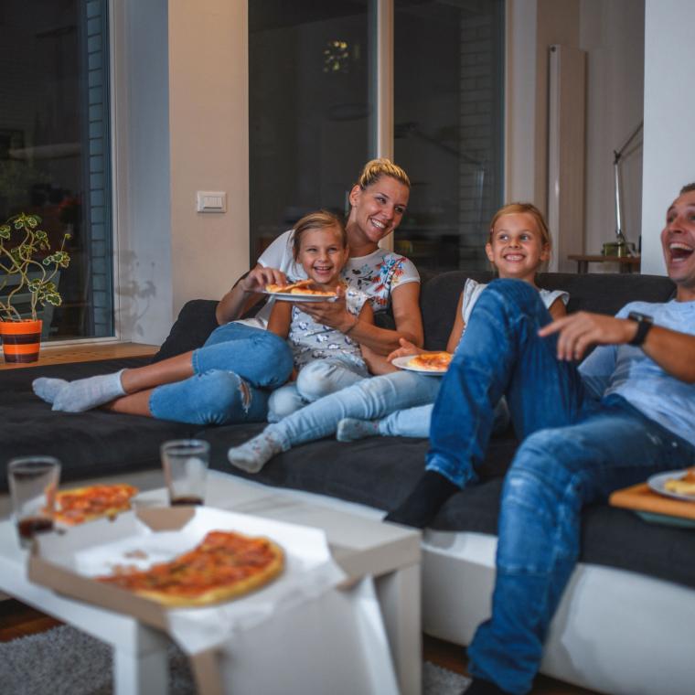 Getty 1271997521 -Caucasian Family Sitting on a Sofa Eating Pizza and Watching TV